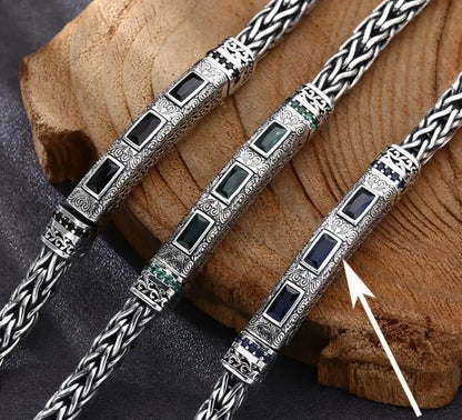 BRAZEN Braided Bracelets with green, blue, and black zirconia stones displayed on wooden surface, showcasing rebellious weave pattern and premium metal detailing